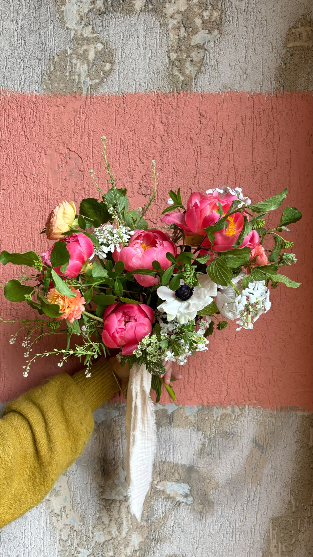 A single 5pm lab bouquet, hand-tied, held against a pink wall