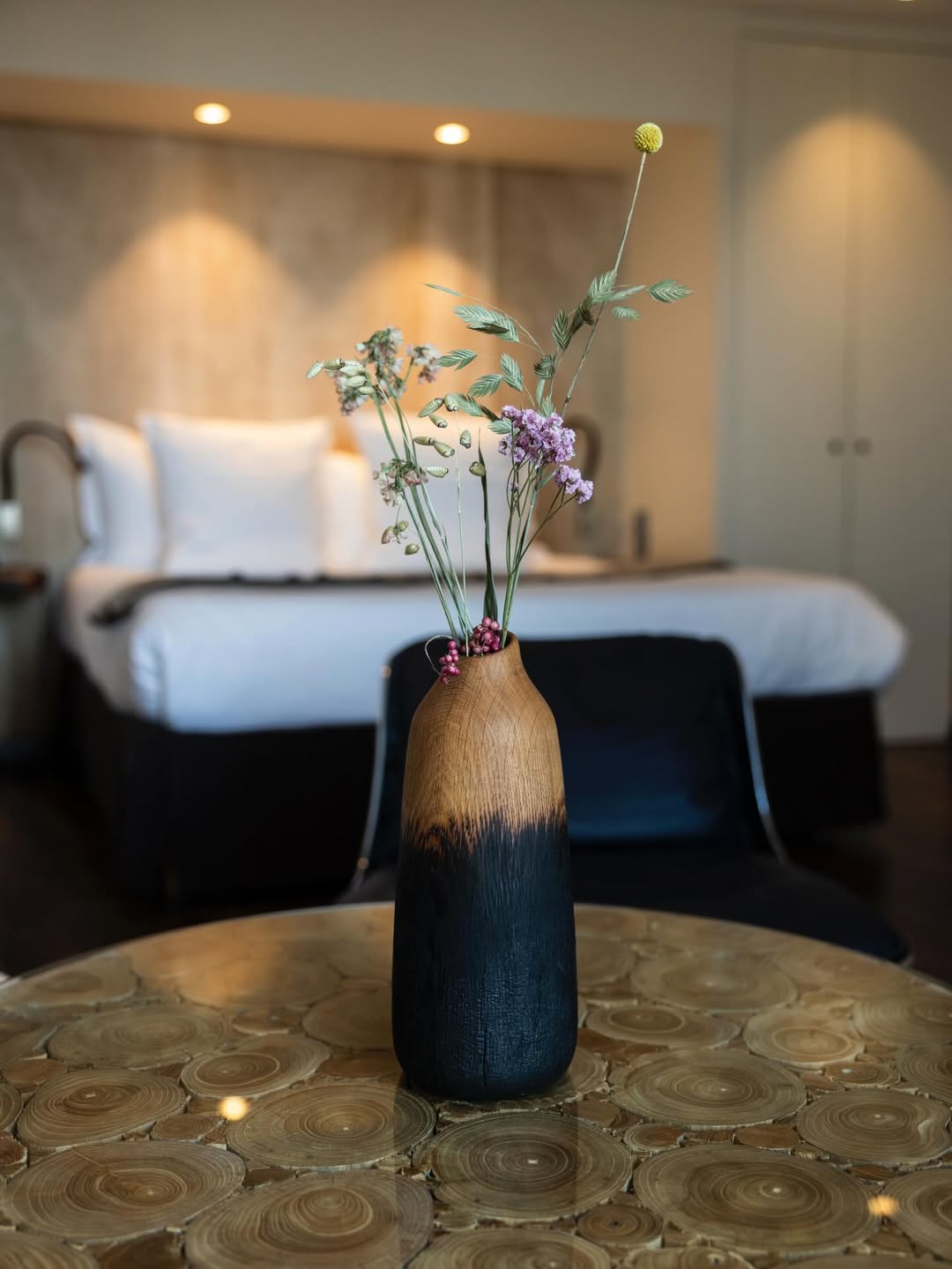 A burnt-oak vase with stems in a calm bedroom